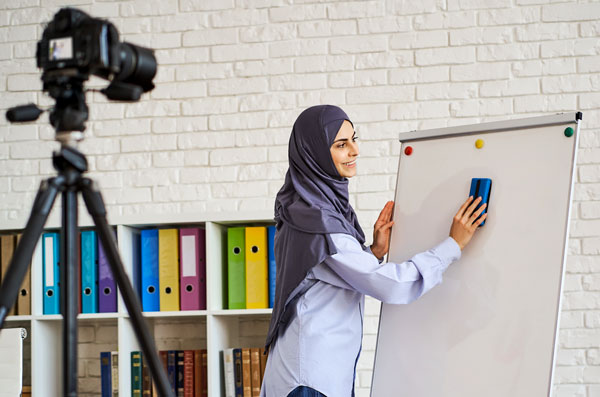 woman wearing headscarf wiping whiteboard in front of camera